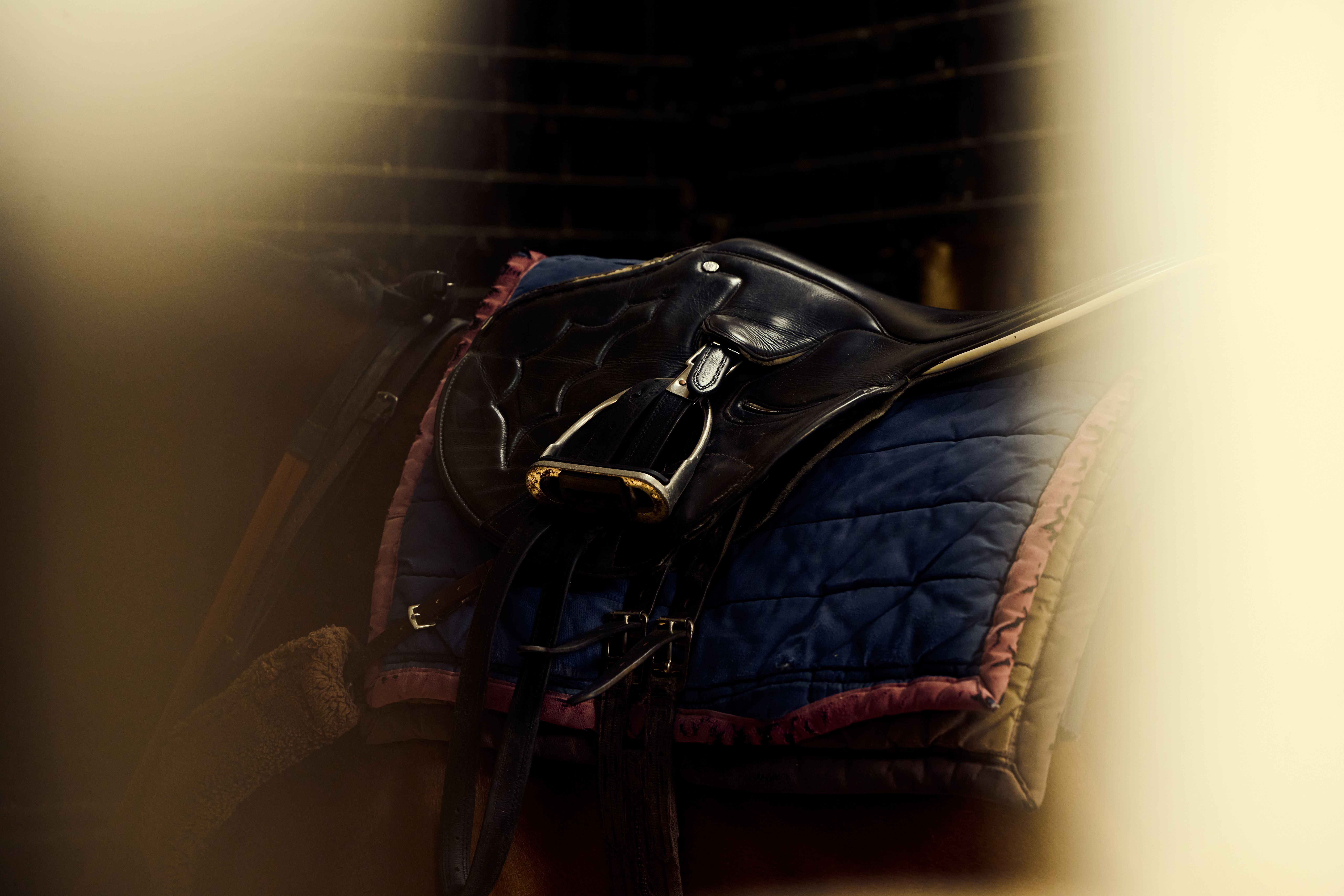 Close-up of a black racing saddle and stirrup on a quilted blue and pink saddle pad